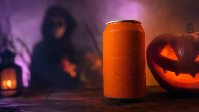Lata de refrigerante em cenário de Halloween com iluminação roxa e laranja e figura mascarada ao fundo.
