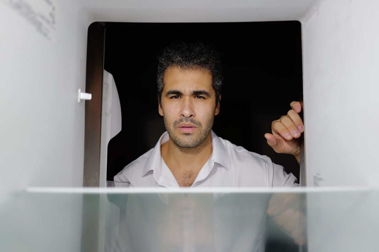 Homem preocupado olha para dentro de uma geladeira vazia em uma cozinha.