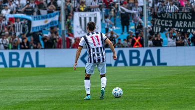 Jogador de futebol com a camisa 11 disputa uma partida diante de torcedores nas arquibancadas.