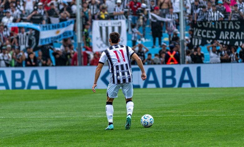 Jogador de futebol com a camisa 11 disputa uma partida diante de torcedores nas arquibancadas.