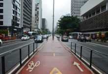 Vista da Avenida Paulista, em São Paulo, com ciclovia, trânsito e edifícios ao redor em um dia nublado.