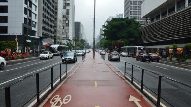 Vista da Avenida Paulista, em São Paulo, com ciclovia, trânsito e edifícios ao redor em um dia nublado.